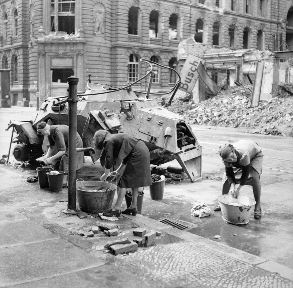 German women doing their washing at a water hydrant in the Französische Straße, near the wreck of a German Leichter Panzerspähwagen, Berlin-Mitte, July 3, 1945