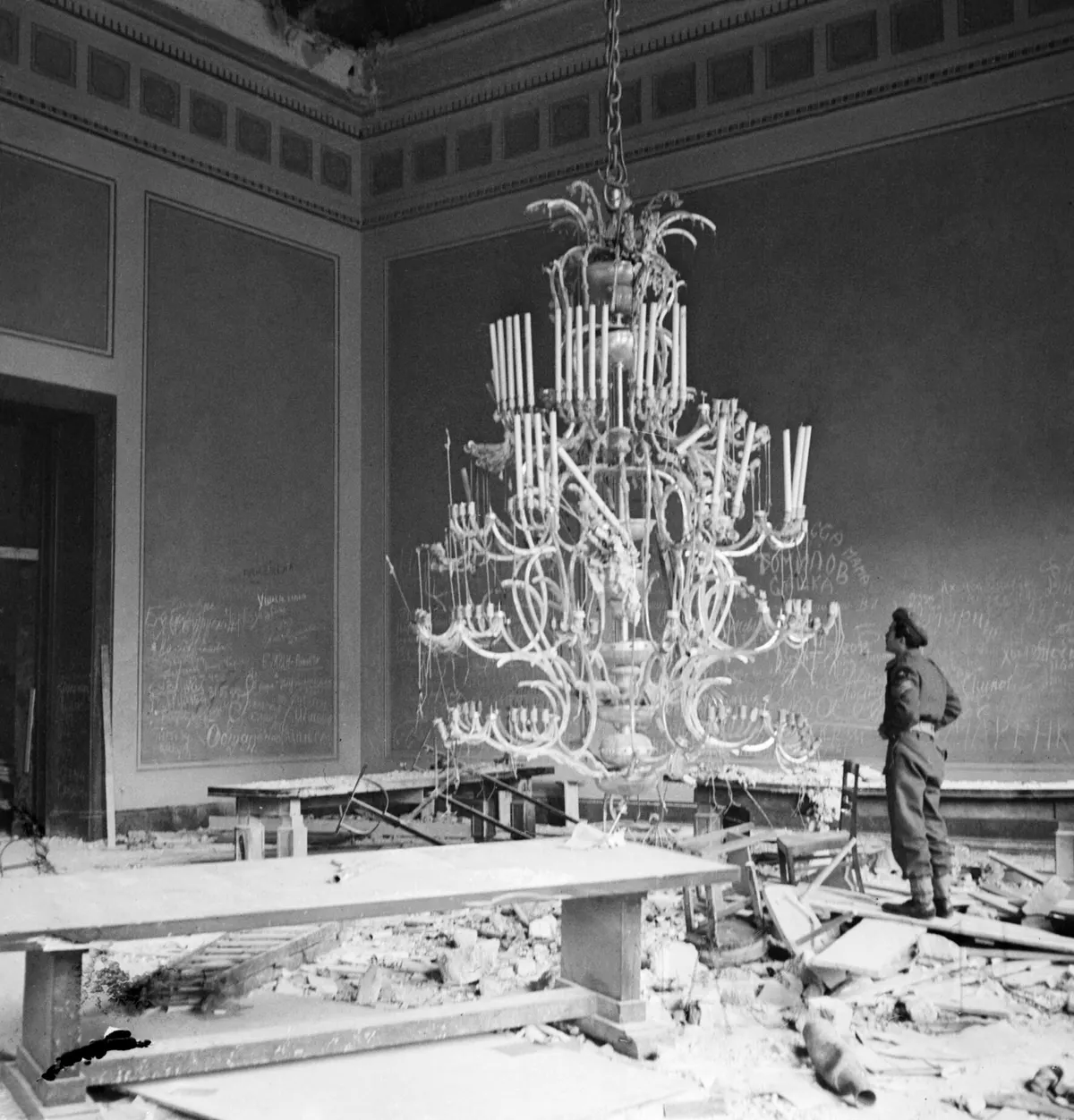 Sergeant R S Baker of the Army Film & Photographic Unit (AFPU) looks at one of the giant chandeliers in the ruins of Hitler's Reich Chancellery in Berlin, 3 July 1945. BU8567
